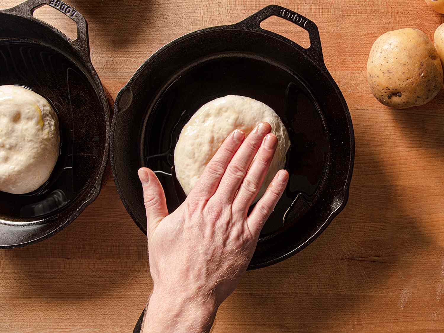 A hand pressing down on a ball of pizza dough inside of a cast iron pan.