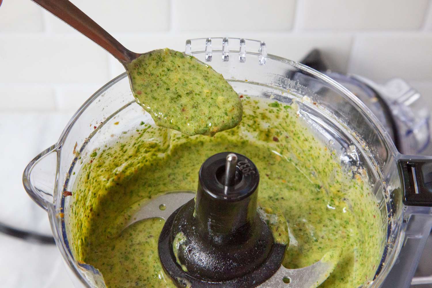 A spoon holding a spoonful of pesto from a mini food processor's bowl.