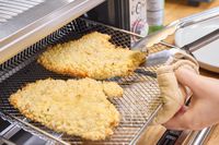 A person removes chicken from the Breville The Smart Oven Air Fryer Compact