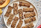 Overhead view of breakfast granola bars on a large plate. The top left has a smaller plate with a broken piece of granola bar on it, and a mug of coffee next to it. 