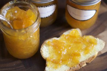 Several jars of honey tangerine marmalade. One has been opened and a piece of toast topped with the marmalade is nearby.