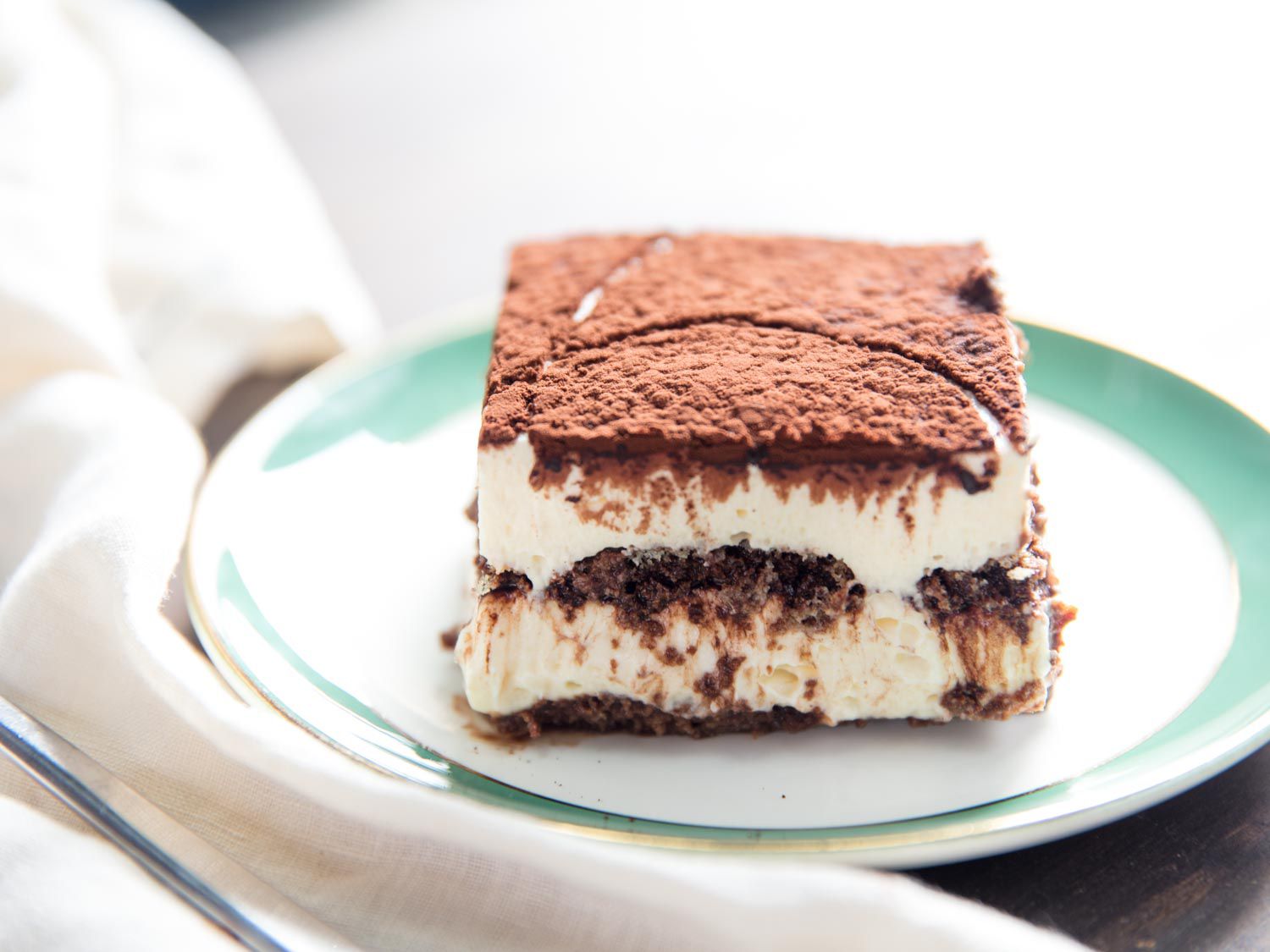A square slice of tiramisu, served on a small light blue plate.