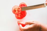 Slicing a tomato on a white cutting board hand holding a Wüsthof knife cutting through a slice