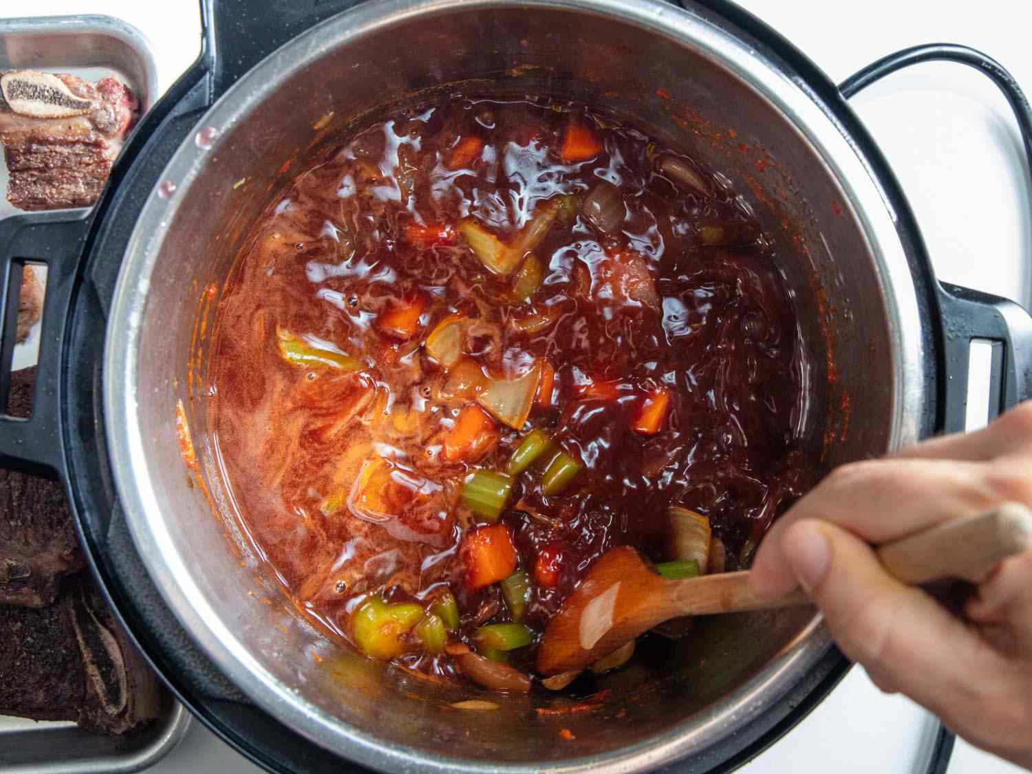 Stirring red wine in the pressure cooker and scraping up browned bits.