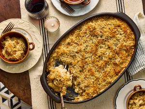 Large dish of French onion soup mac and cheese, with 2 cups of servings on dishes, a candle, a striped tablecloth