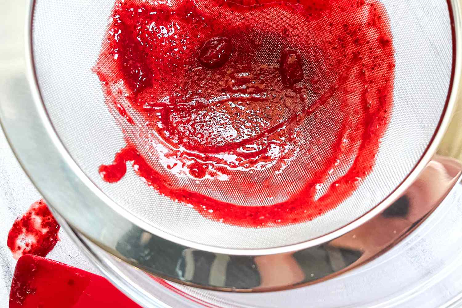 Rösle Stainless Steel Round Handle Kitchen Strainer containing strained red puree or sauce over a bowl