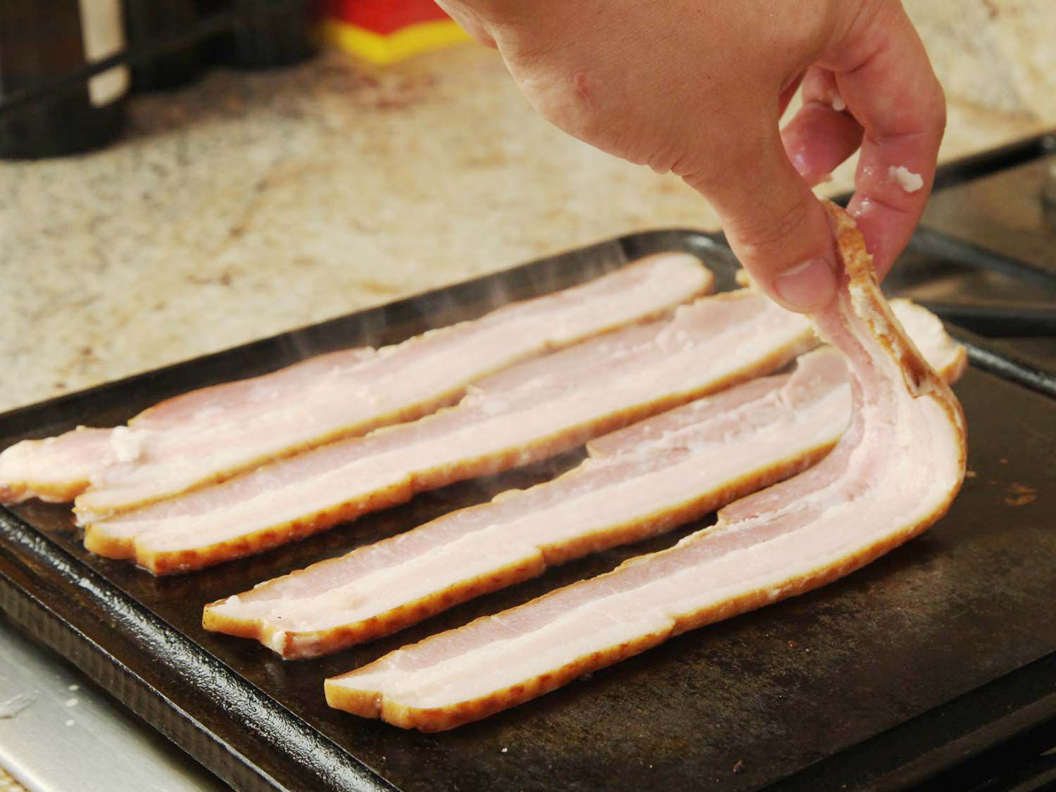 Cooked bacon is arranged on a griddle to brown.