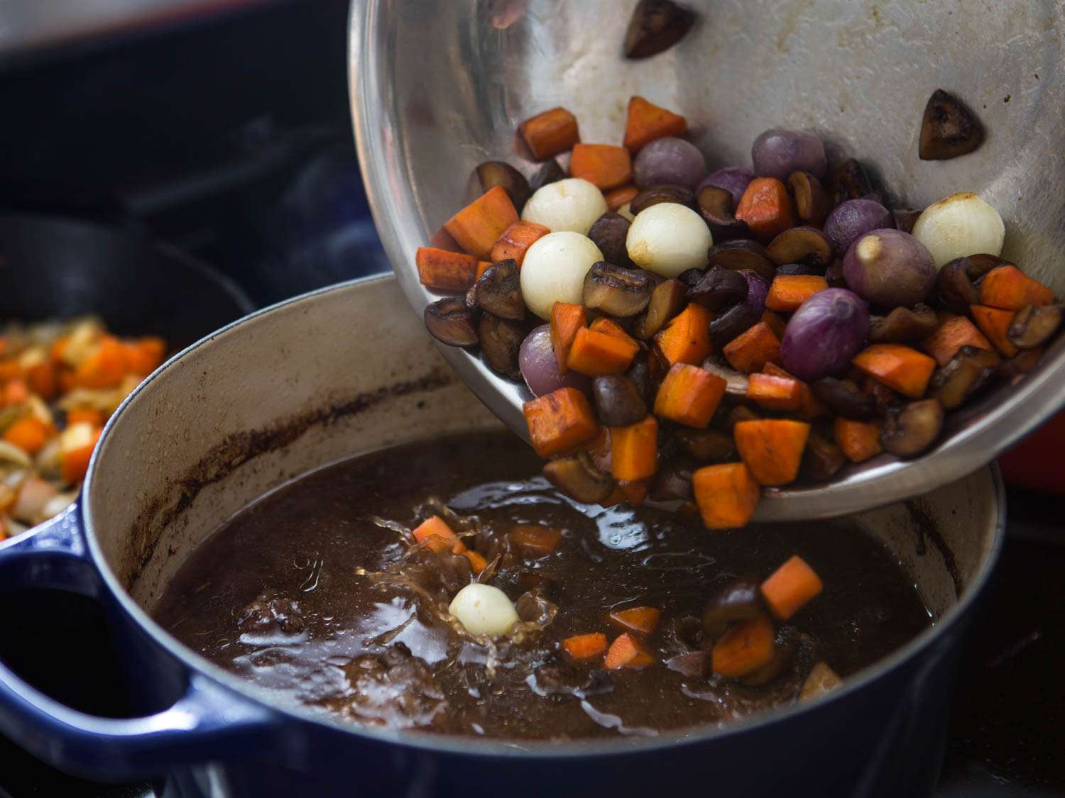 Adding saute vegetable and aromatics into boeuf Bourguignon pot. 