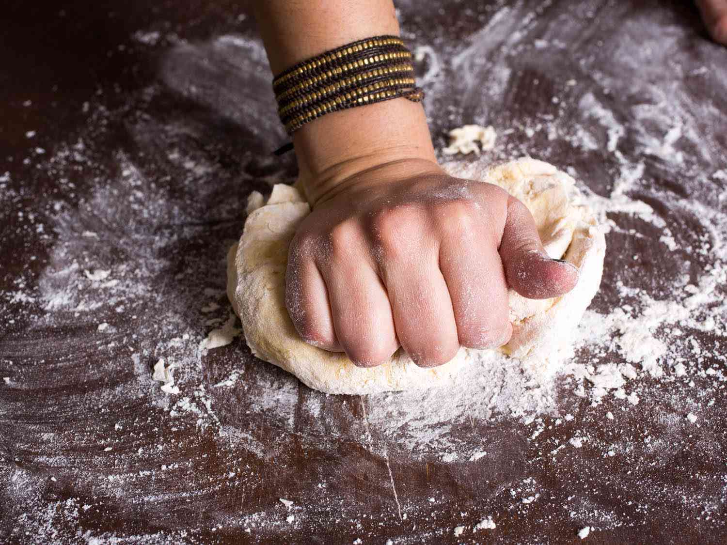 Kneading the pasta dough by pressing the heel of your hand into the ball of dough, pushing forward and down. 