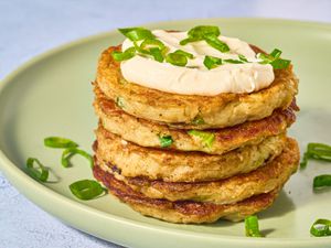 stack of boxty pancakes with dollop on sourcream, and garnished with green onions on a green place on stone surface.
