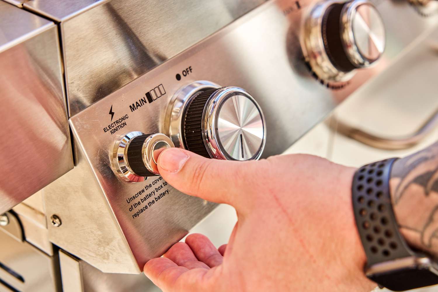 Hand pressing a button on the Monument Grills Stainless 4-Burner Propane Gas Grill