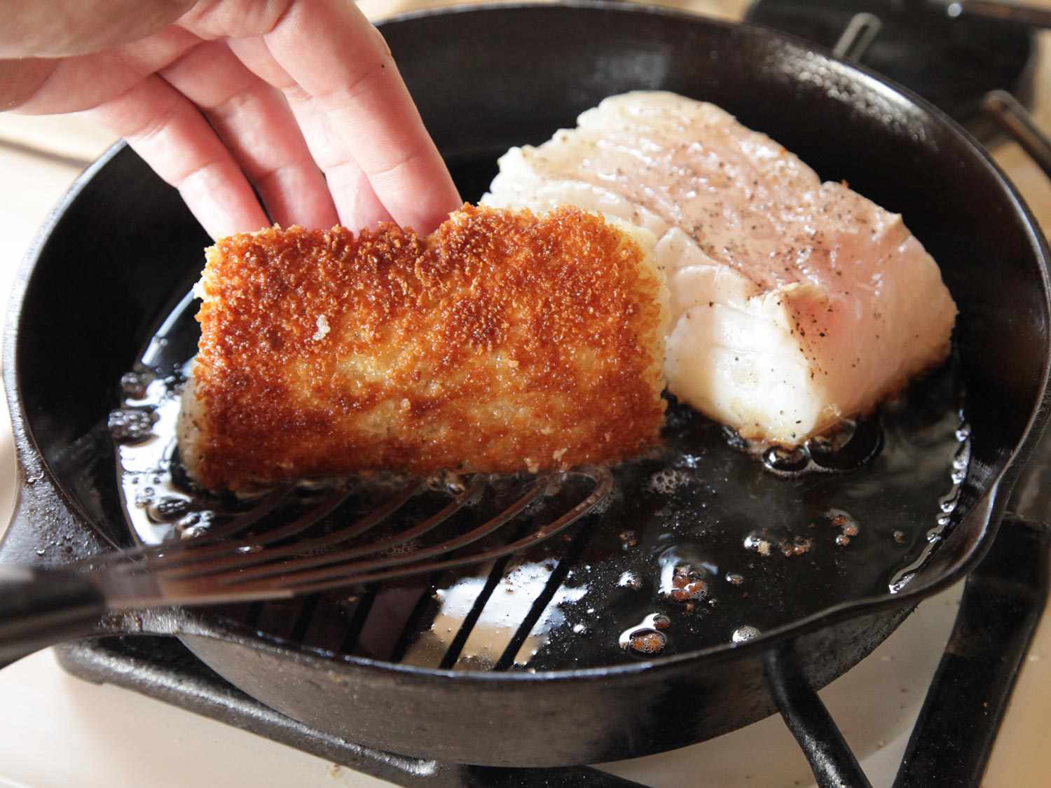 Turning a piece of fish in a cast iron skillet with a fish spatula to show the crispy breaded side. 