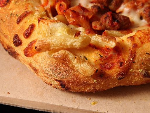 An edge of Domino's bread bowl pasta with some penne stuck on the outside crust. The penne's been toasted with the pizza dough.