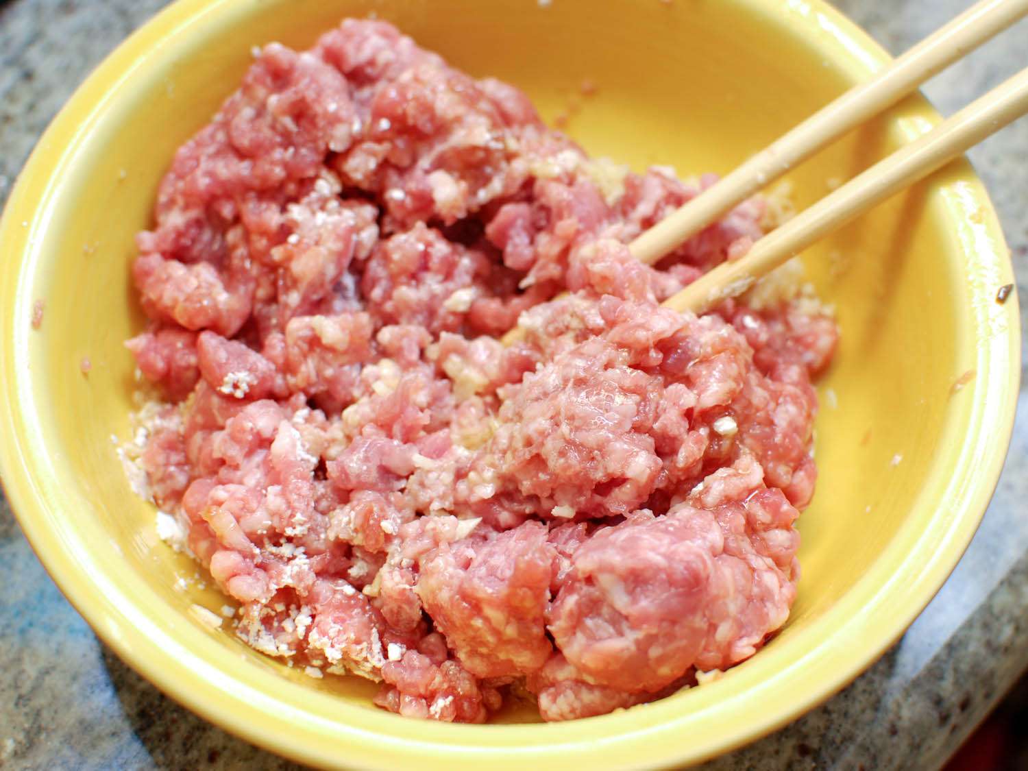 Combining pork and seasoning in a mixing bowl. 