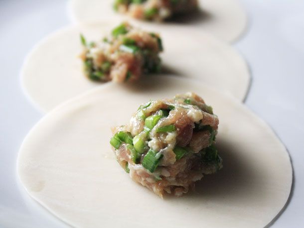 Close-up of several round dumpling wrappers with a scoop of pork and chive filling resting in their center.
