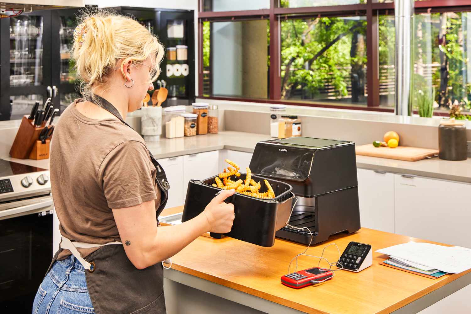 A person tossing fries inside of the Cosori Pro II 5.8 Quart Air Fryer Oven Combo basket