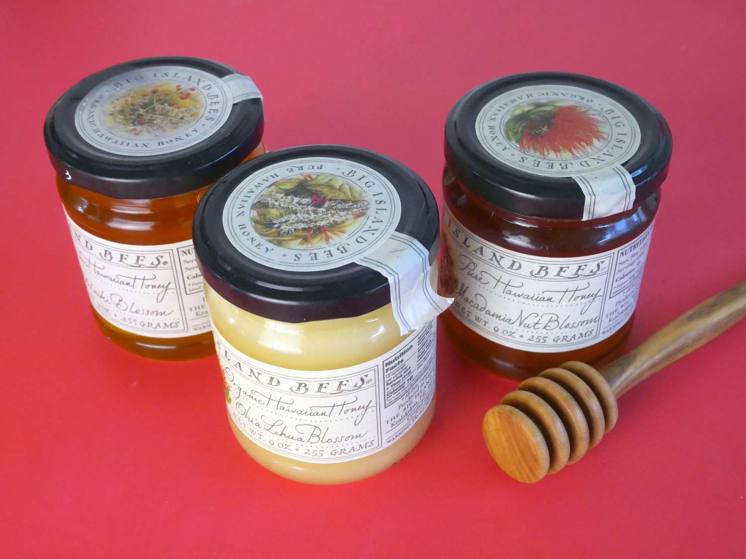big island bees three jars of honey on red surface with honey dripper