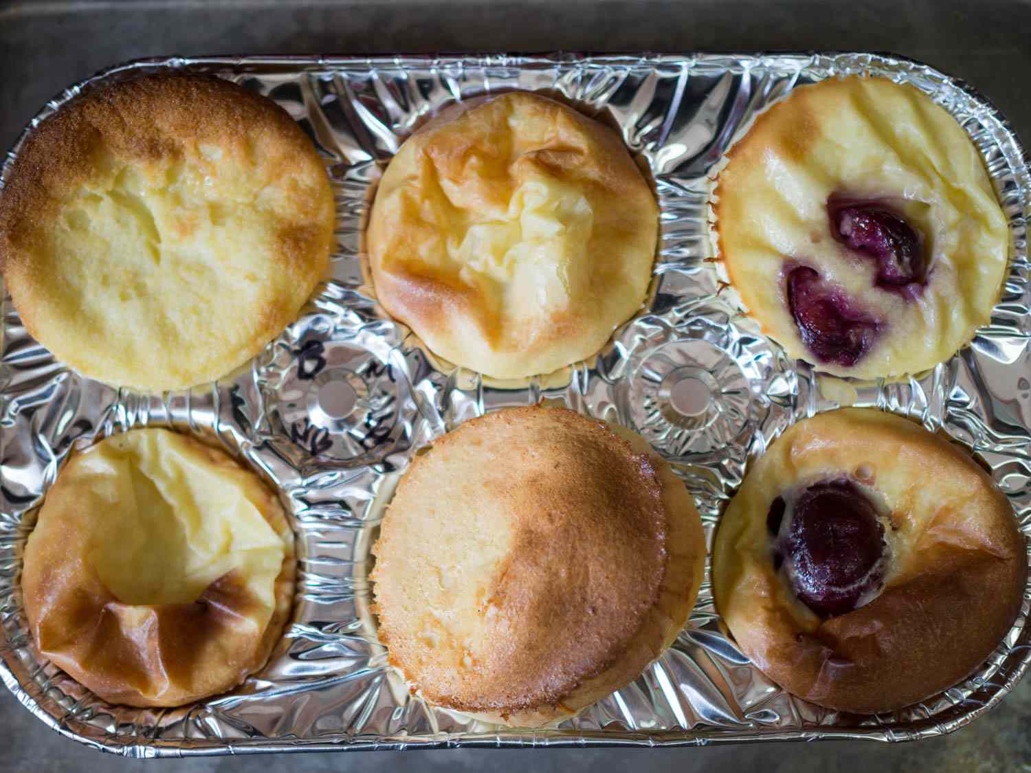 Testing cherry clafoutis batter in a six-cup muffin tin: Top left, with butter; bottom left, without butter. Top center, with milk; bottom center, with half and half. Top right, pitted cherry; bottom right, whole cherry.