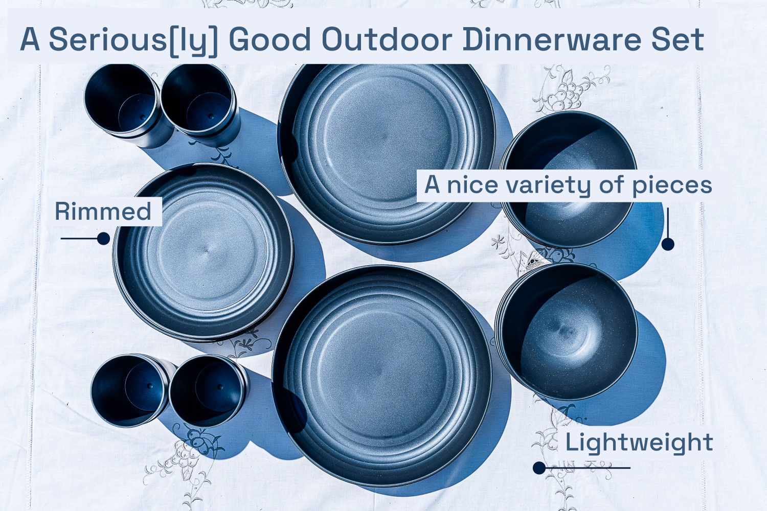 An overhead view of a dark blue outdoor dinnerware set over a white patterned tablecloth 