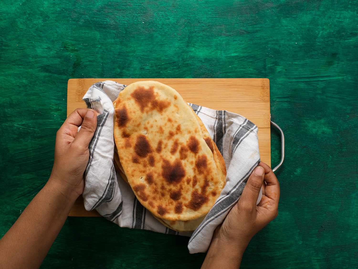 Naan wrapped together in striped towel on wooden board 