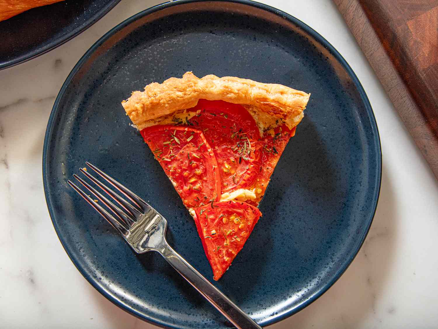 A slice of tomato tart on a plate with a fork