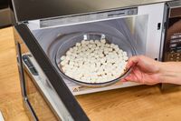 A hand placing a bowl of marshmallows into the Toshiba EM131A5C-BS Microwave Oven