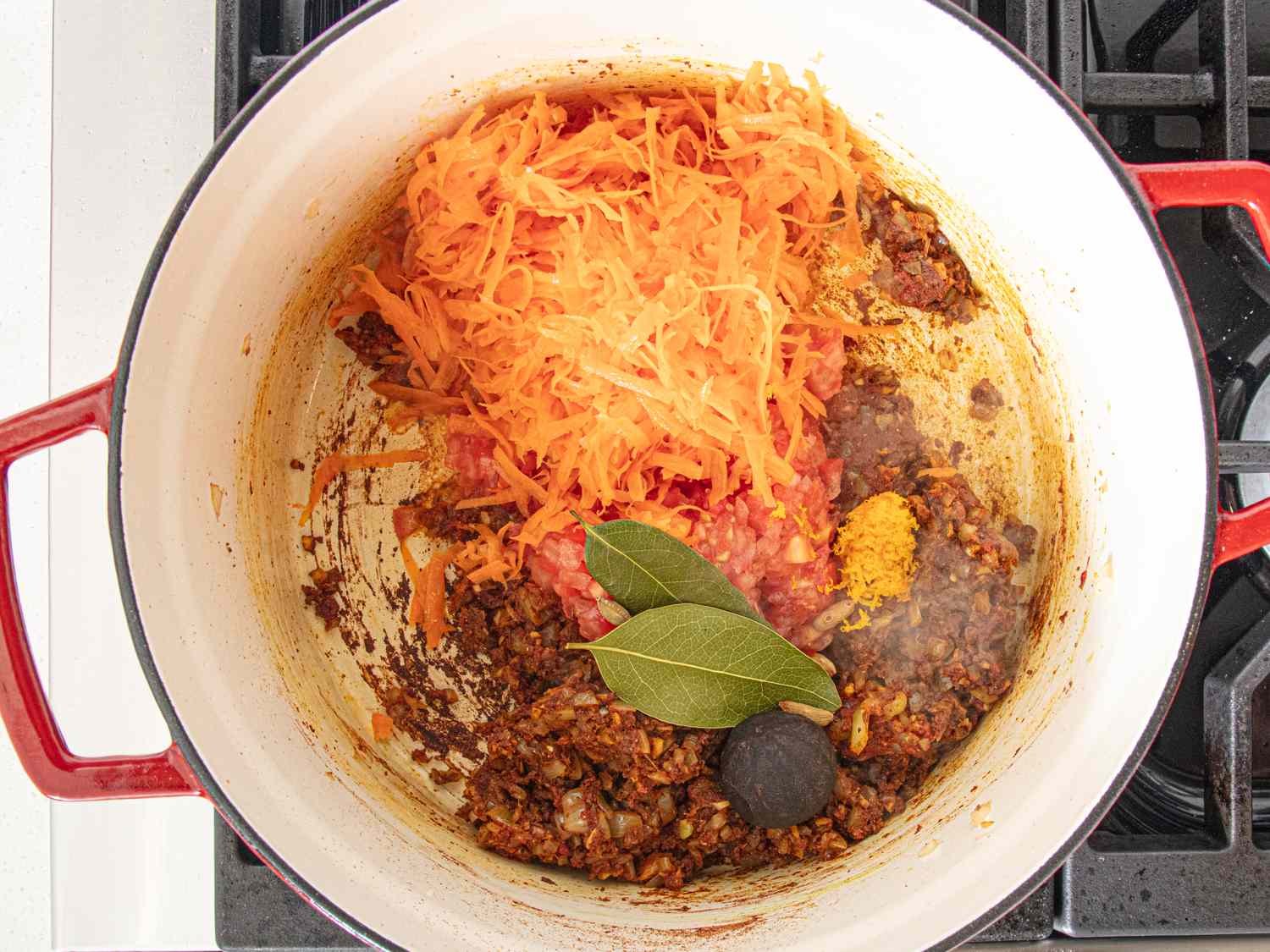 A pot containing ingredients for a dish including shredded vegetables spices bay leaves and sauted ingredients