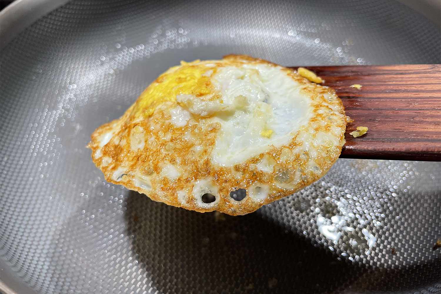 A cooked egg on a wooden spatula above a textured pan