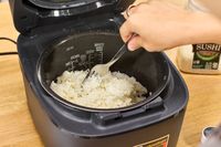 A person fluffs rice cooked in the Zojirushi NW-QAC10 Induction Heating Rice Cooker & Warmer with a fork