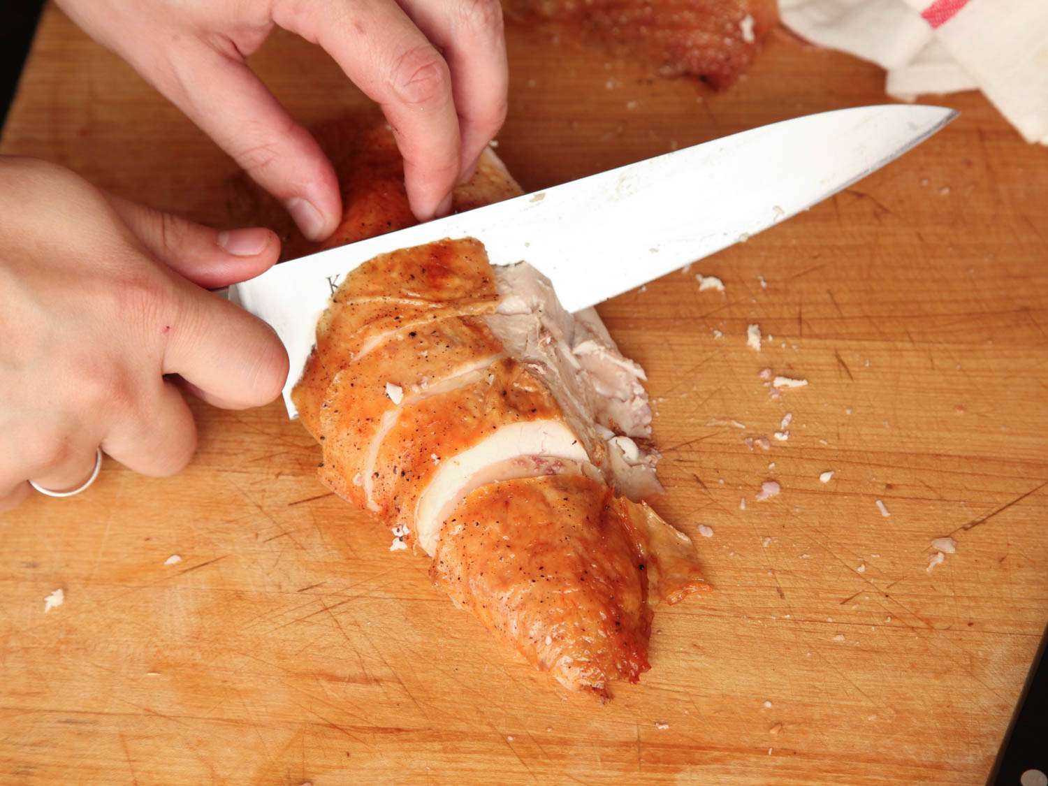 A person slicing cooked turkey breast on a wooden cutting board