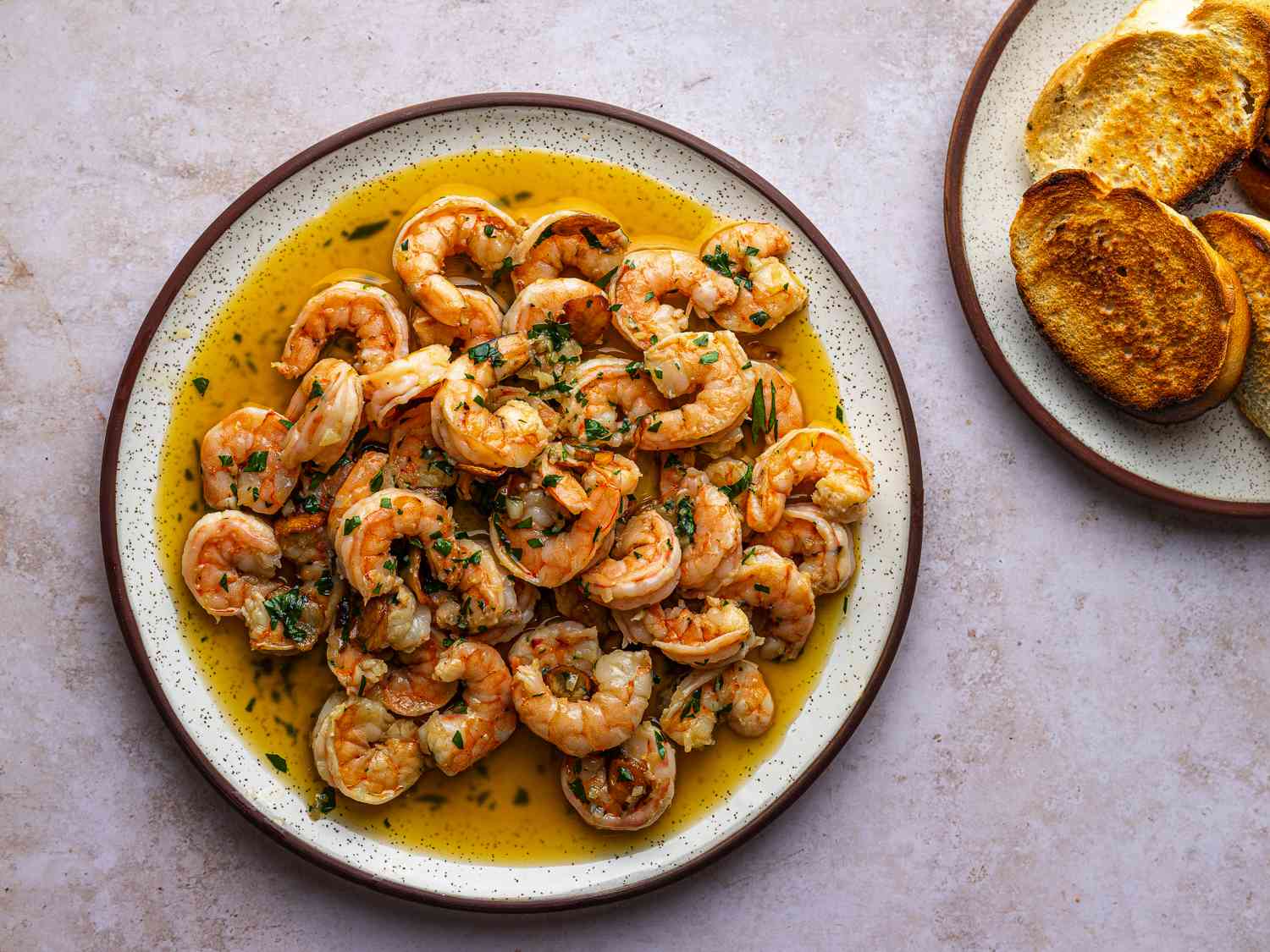 A plate of Spanish-Style Garlic Shrimp (Gambas al Ajillo). On the right hand side of the image is a smaller plate of toasted bread.