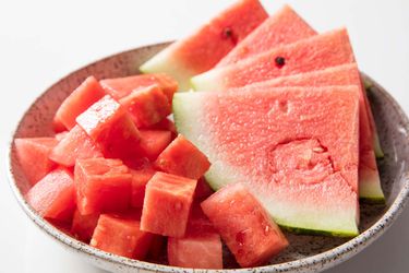 A bowl holding cubed watermelon and five watermelon wedges.
