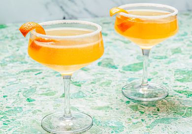 Two sidecar cocktails in stemmed cocktail glasses with sugared rims and an orange peel garnish 