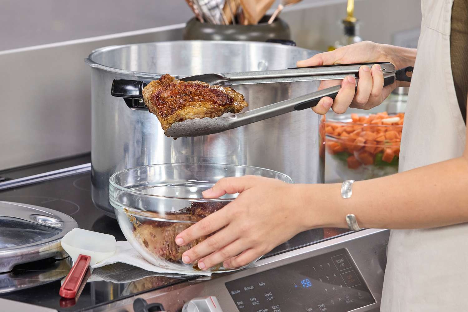 A person transferring a cooked piece of meat from the Presto 16-Quart Pressure Canner and Cooker into a glass bowl