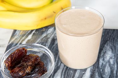 A bananadate smoothie in a glass bananas and dates beside it