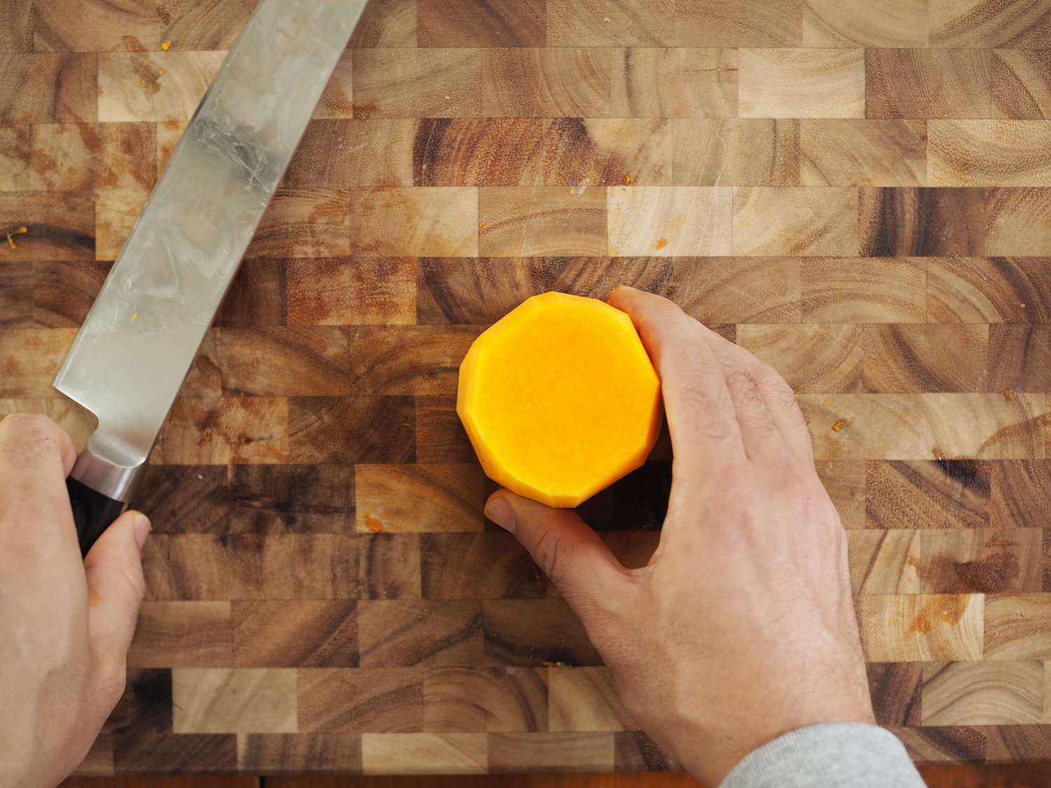 A hand holding a round slice of butternut squash neck.