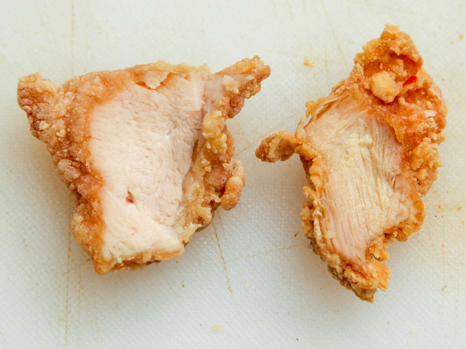 Fried chicken breast (left) and fried chicken thigh (right) side-by-side on white cutting board.
