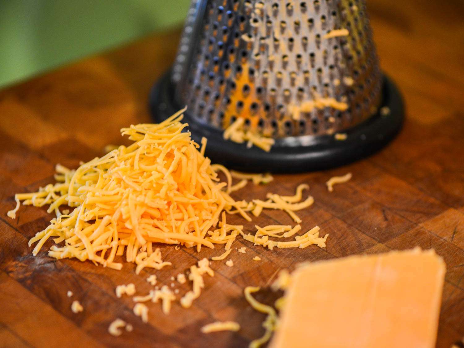 A block of cheddar cheese grated on a box grater.