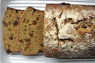 Overhead view of a freshly baked sticky malt loaf, served on a ridged platter. Two slices have been cut and shingled to reveal the interior texture of the quick bread.