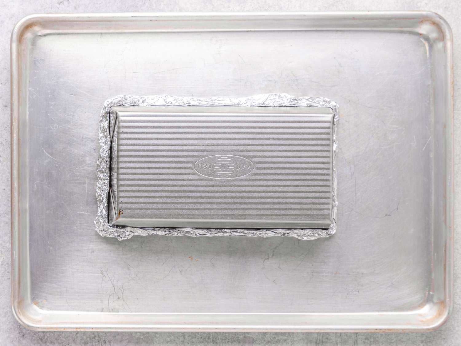 A loaf pan covered with foil on a baking sheet
