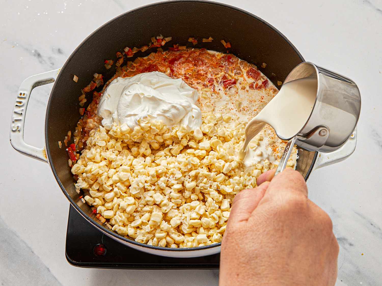 Cream and sour cream being added to a pot of cooked corn on a stovetop