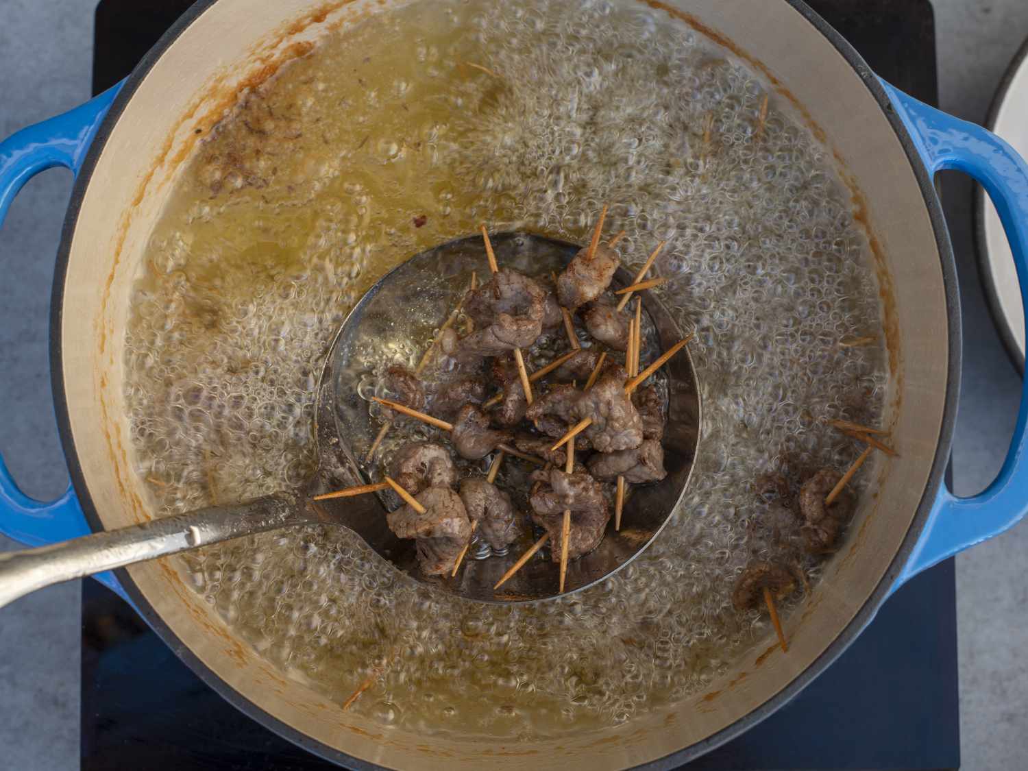 Strainer lifting deep fried toothpick lamb out of frying oil in a Dutch oven