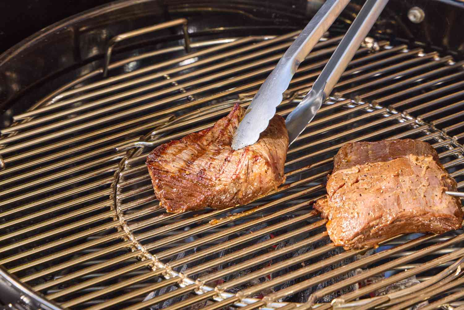 Tongs touching meat on the Weber Performer Deluxe Charcoal Grill 22