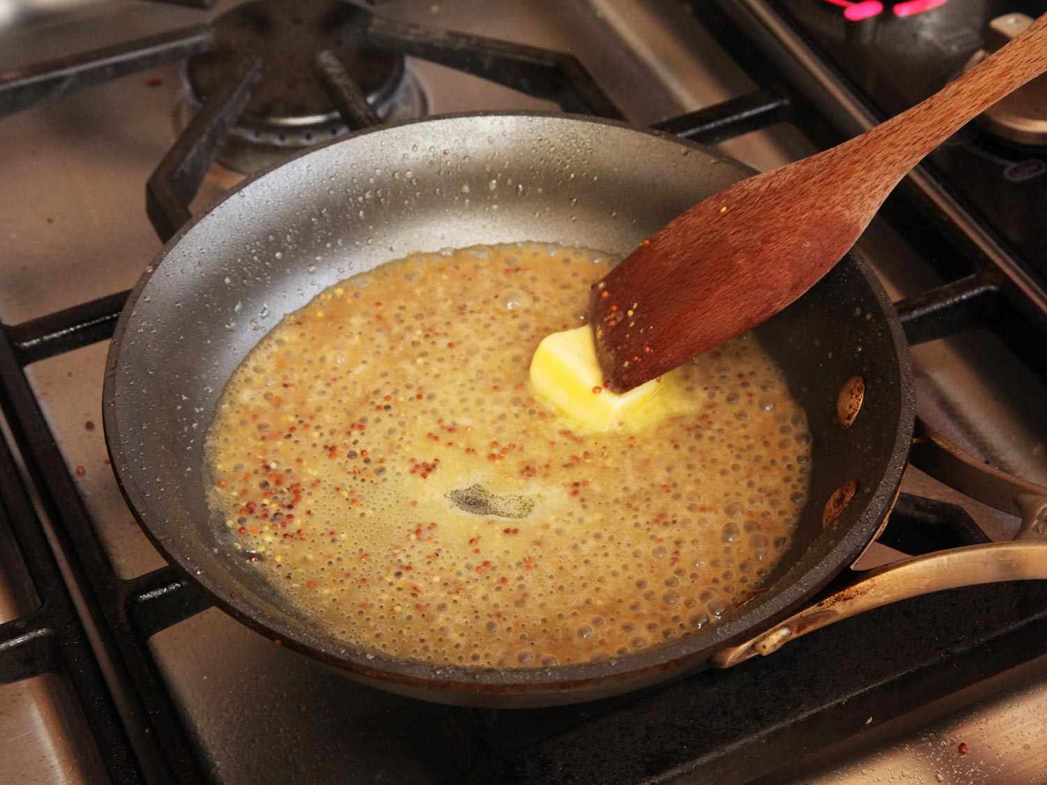 Stirring butter into a mustard pan sauce in a skillet.