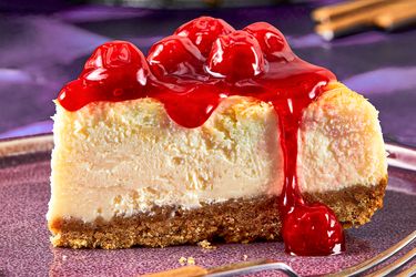 Slice of cheesecake topped with cherry topping on a plate with a fork nearby