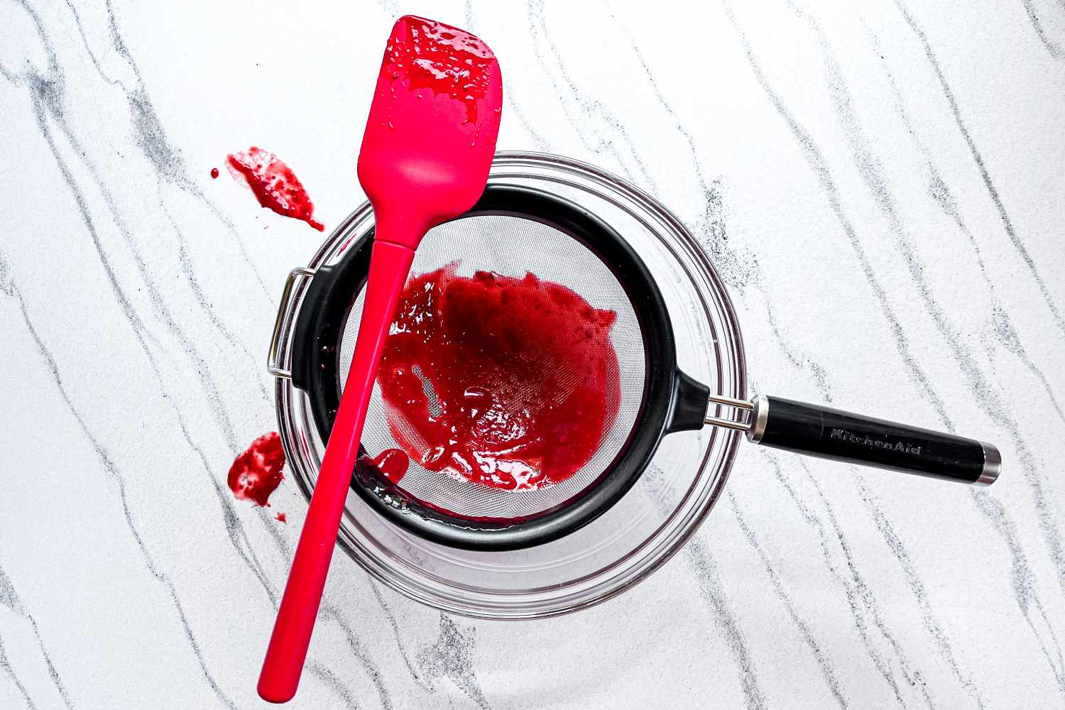 KitchenAid Classic Strainer with a red spatula and red liquid in a mixing bowl on a white surface