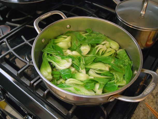 Baby bok choy blanching in a large pot of water.