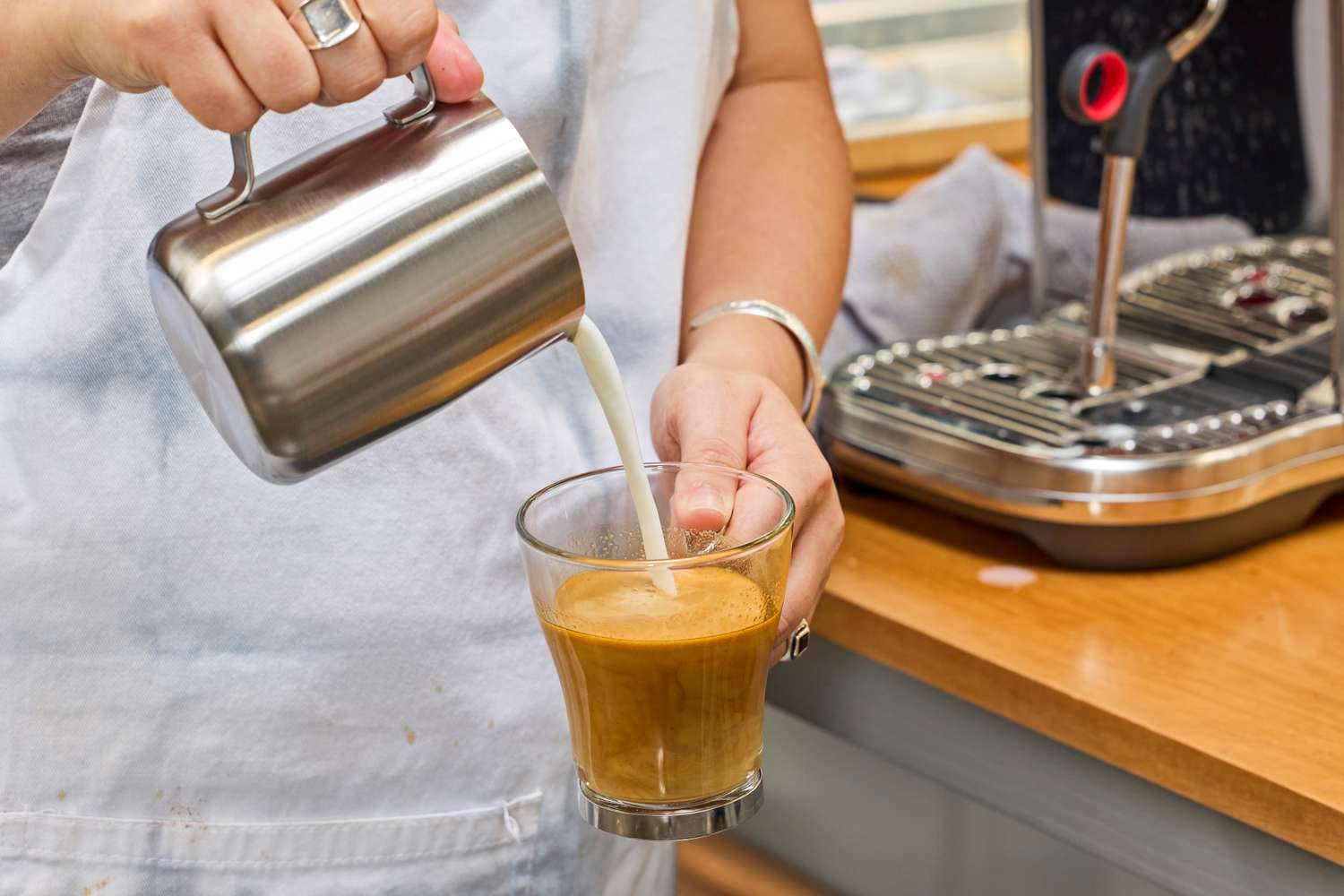 A person pouring steamed milk in a cup of espresso
