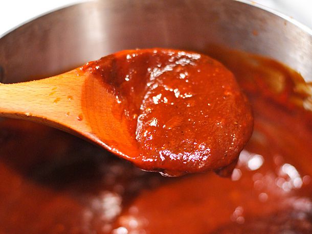 Cooking homemade Kansas City-style barbecue sauce in a pot. A wooden spoon holding sauce is being held up over the pot.