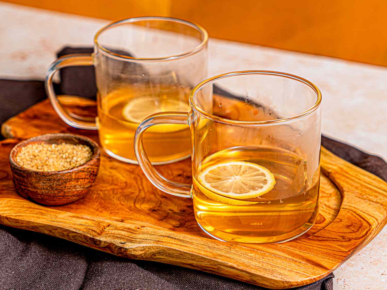 Two hot toddies served on a wooden board with lemon slices, next to a small bowl of demerara sugar
